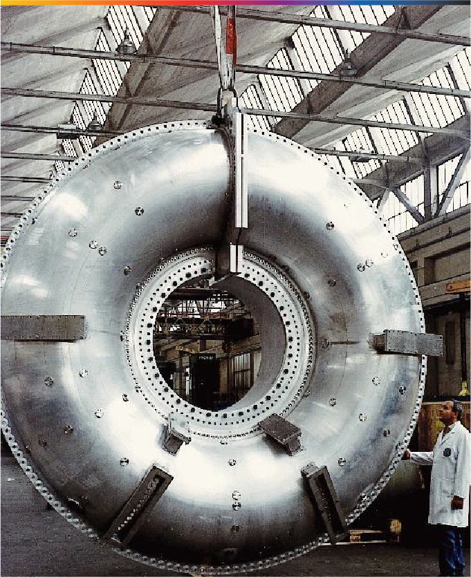 A large metal donut is suspended from the ground, and a person wearing a lab coat stands next to it.