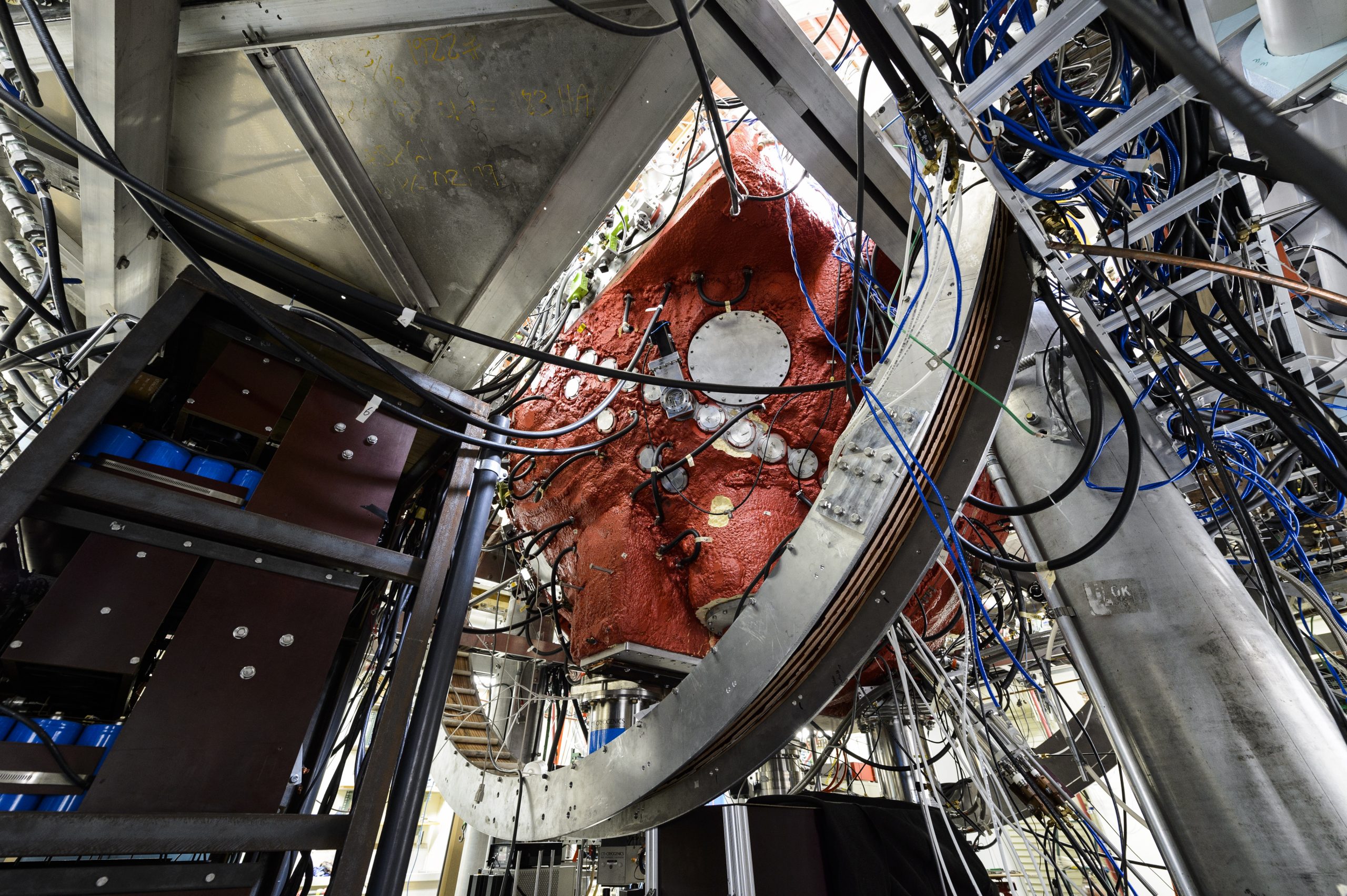 A large spherical device being suspended with metal supports, with wires, sensors, and hatches covering it.