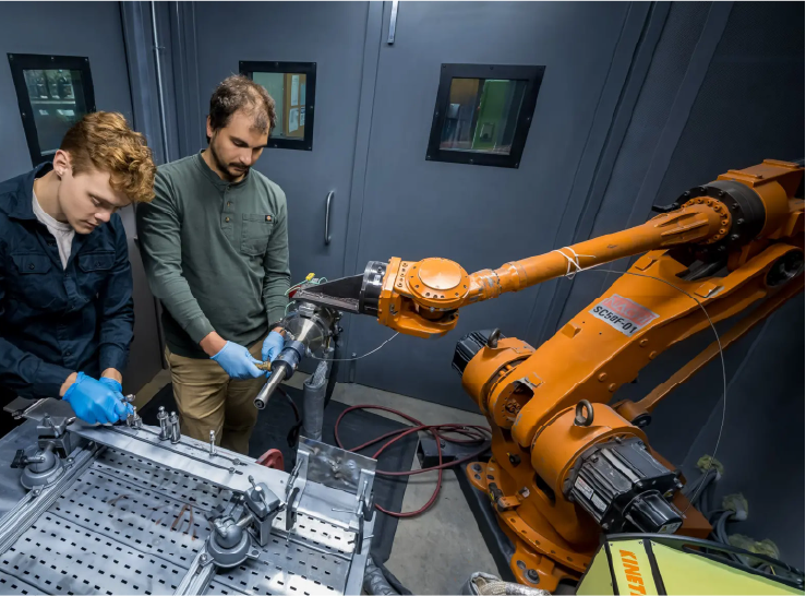 Two people monitor a large orange, arm-like device.