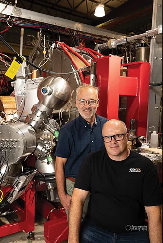 two white men stand beside a large piece of fusion science equipment