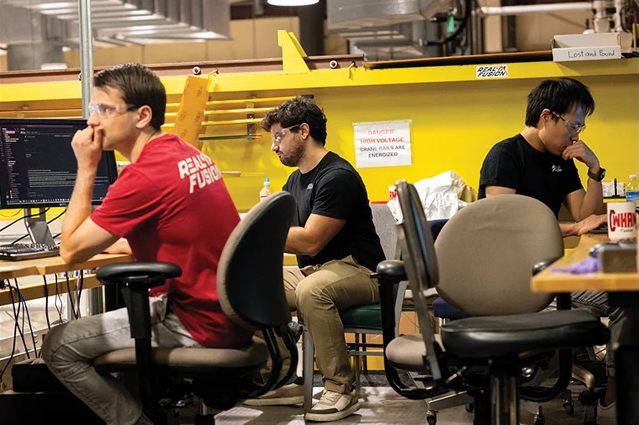 three people sit in near computers in a lab