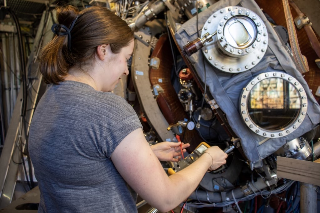 person working closely on a large piece of scientific equipment