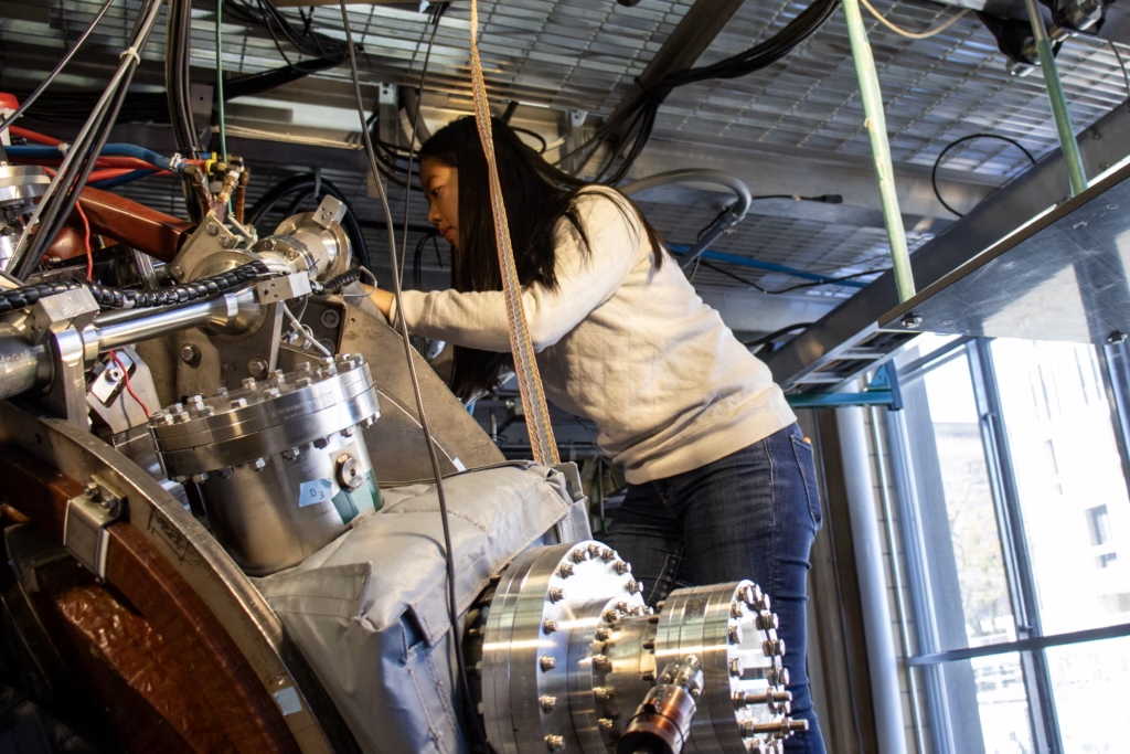 person working closely on a piece of scientific equipment, on a ladder