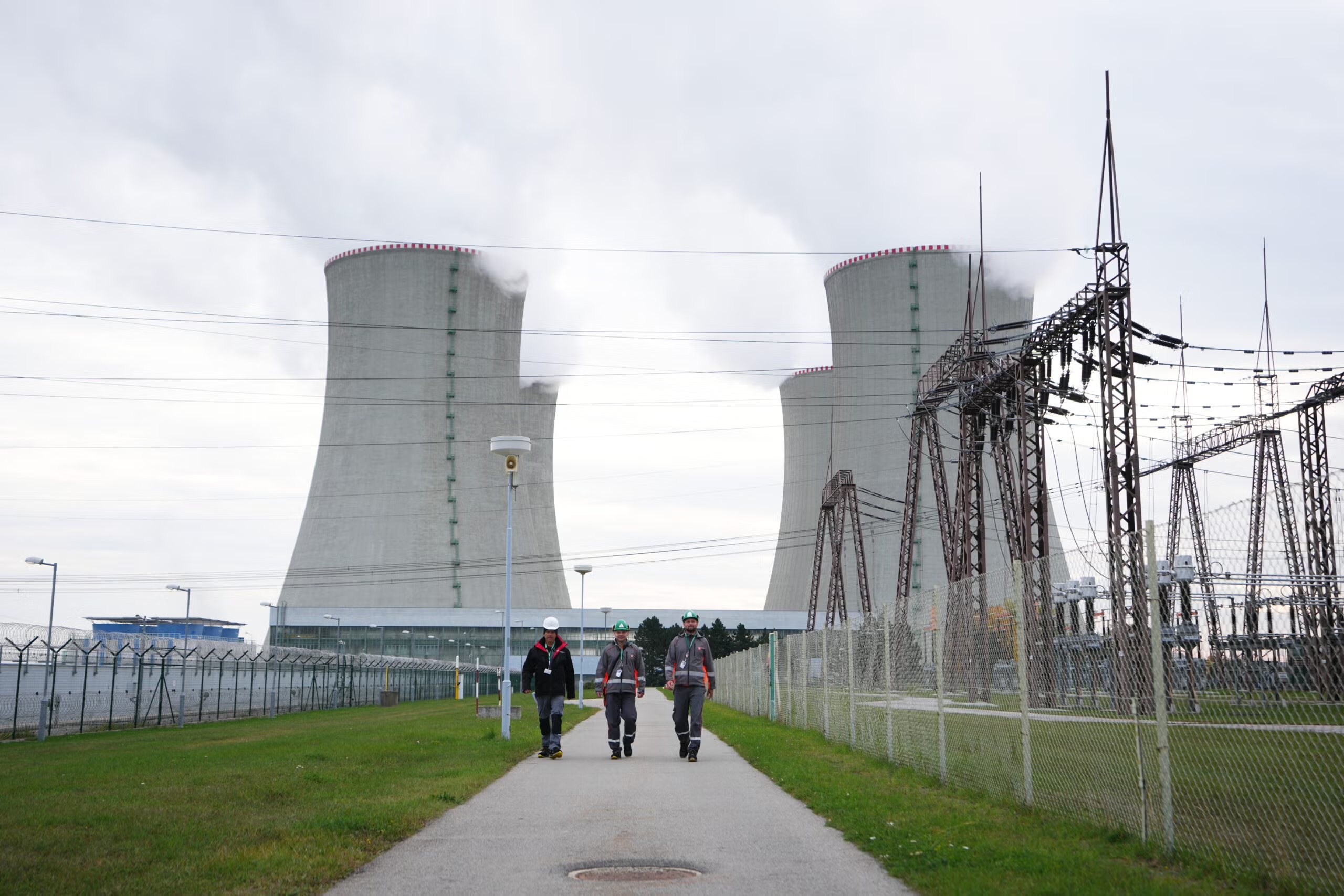 three people walking in front of a nuclear power plant with towers