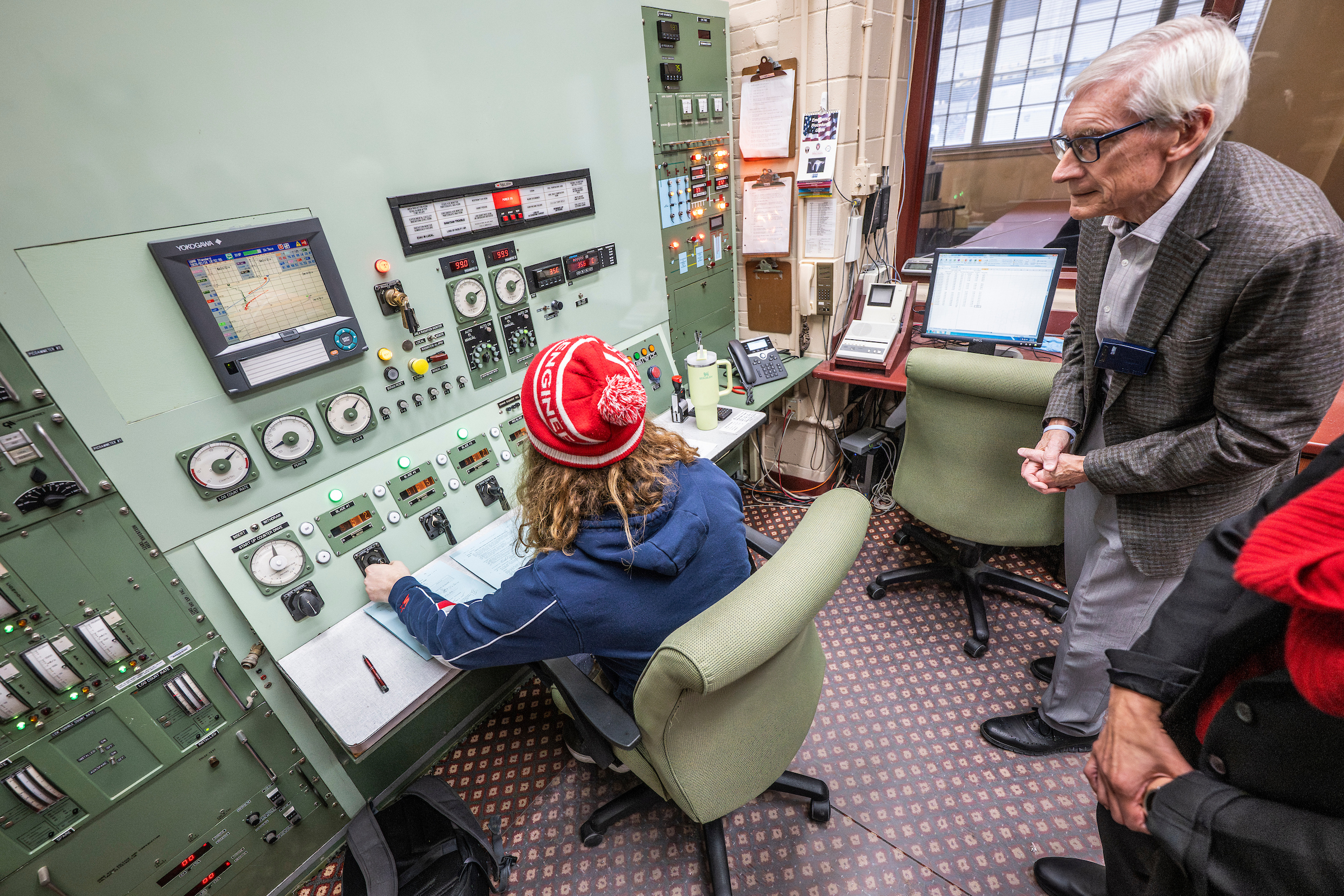 person sitting at a large control panel showing another two people how it works