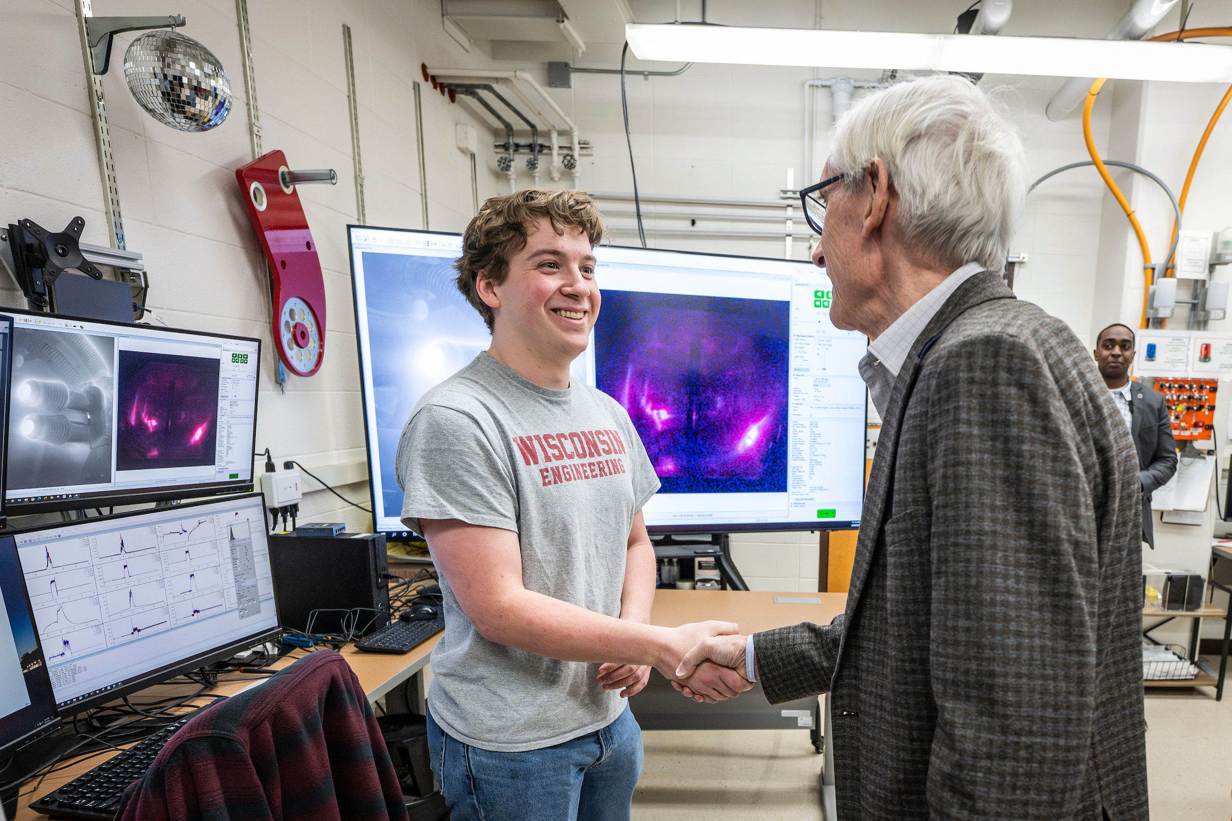 a man with short gray hair shakes the hand of a young man with short blond hair