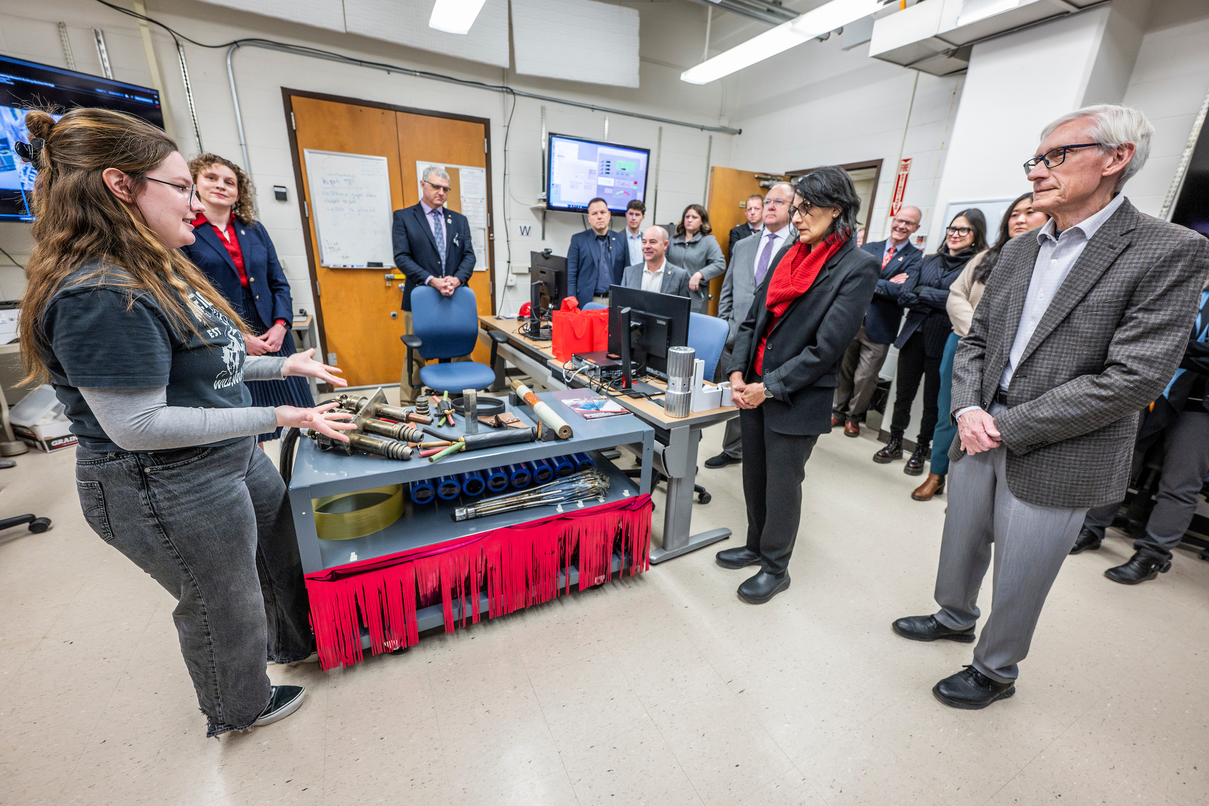 a young person addresses a small group of people in a computer lab room