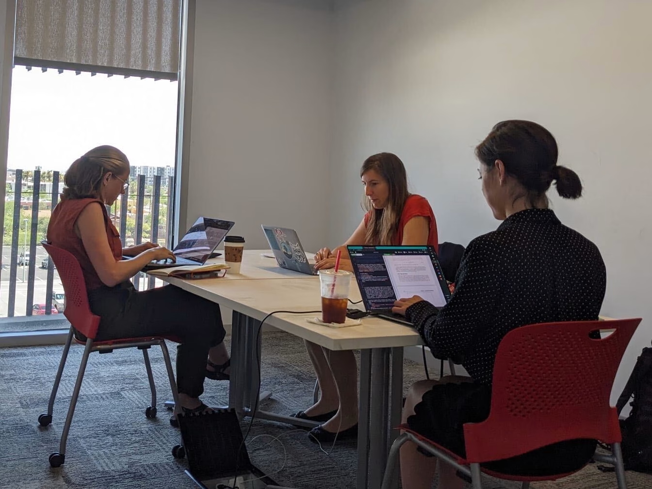 three women around a table working at laptops