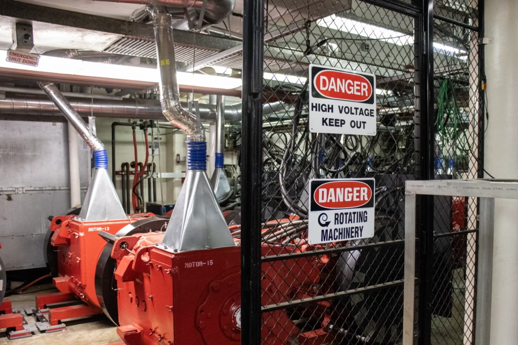 warning and danger signs attached to a wire fence, with pieces of equipment behind it