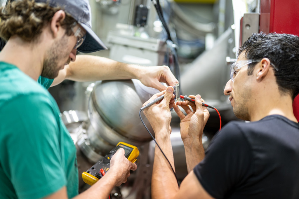 two men work with a piece of wiring on a larger scientific machine
